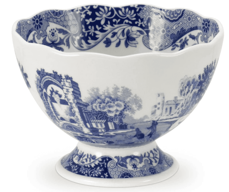A decorative porcelain bowl with a fluted edge, adorned with blue and white traditional pastoral scenes and floral patterns. Perfect for your Saturday shopping finds, the intricate designs depict buildings, trees, and people in a classic, scenic outdoor setting.